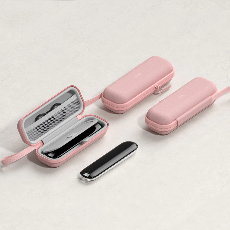 Three pink hard-shell travel cases with straps are arranged on a light neutral background. One case is open, showing a black rectangular item inside, and a slim black-and-silver accessory lies in front.