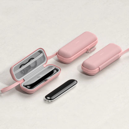 Three pink hard-shell travel cases with straps are arranged on a light neutral background. One case is open, showing a black rectangular item inside, and a slim black-and-silver accessory lies in front.