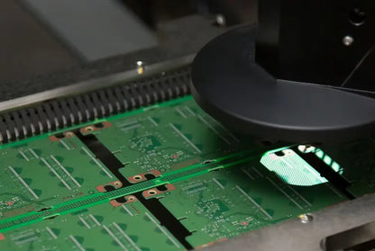 Close-up of a green printed circuit board under inspection by a black automated inspection probe inside a manufacturing facility.