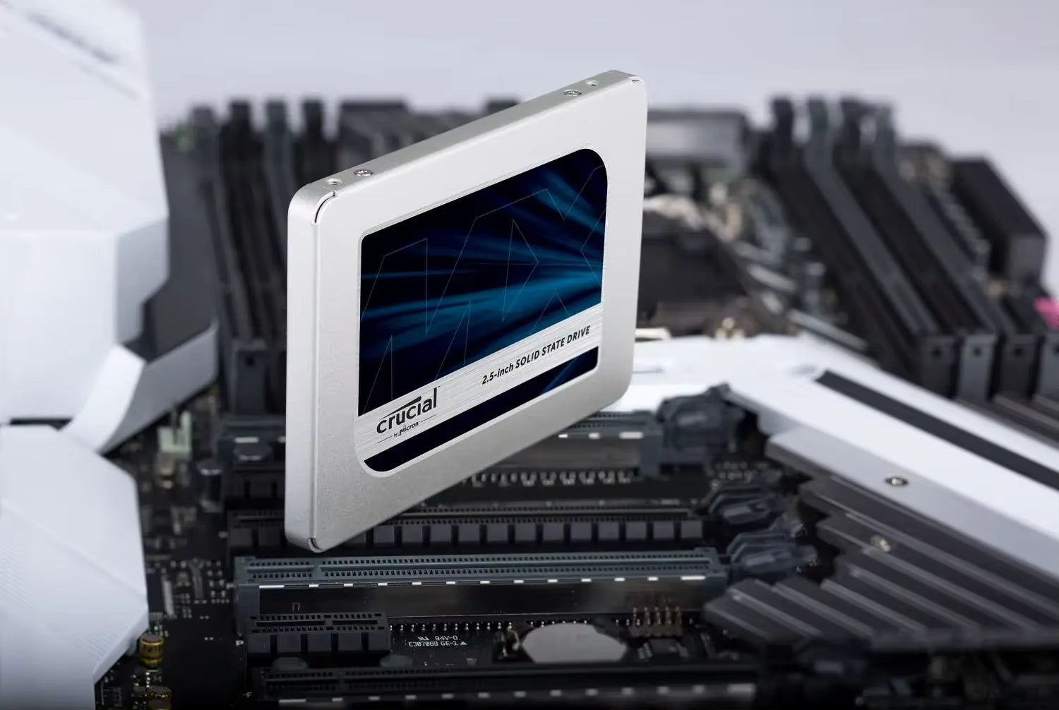 A Crucial 2.5-inch SSD shown floating above a motherboard, highlighting its silver metal casing and blue graphic display window.