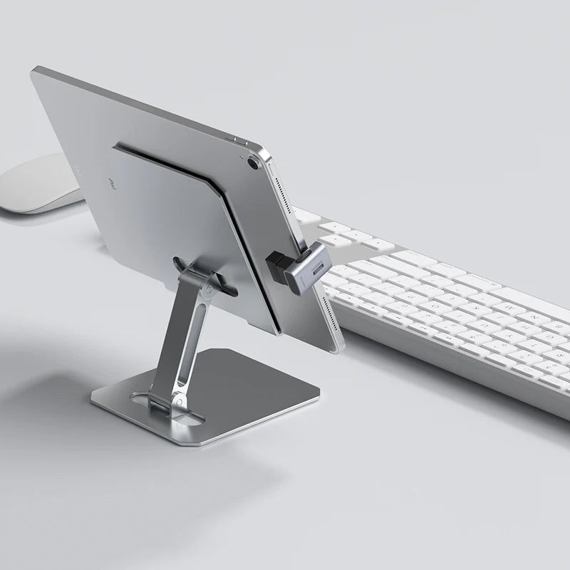 Metallic tablet stand holding a tablet next to a keyboard on a light gray surface